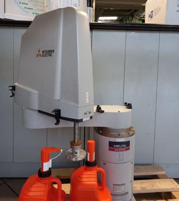 Robot Mitsubishi Electric. Macchina grigia, brocche arancioni, base cilindrica bianca, sfondo di pallet di legno.