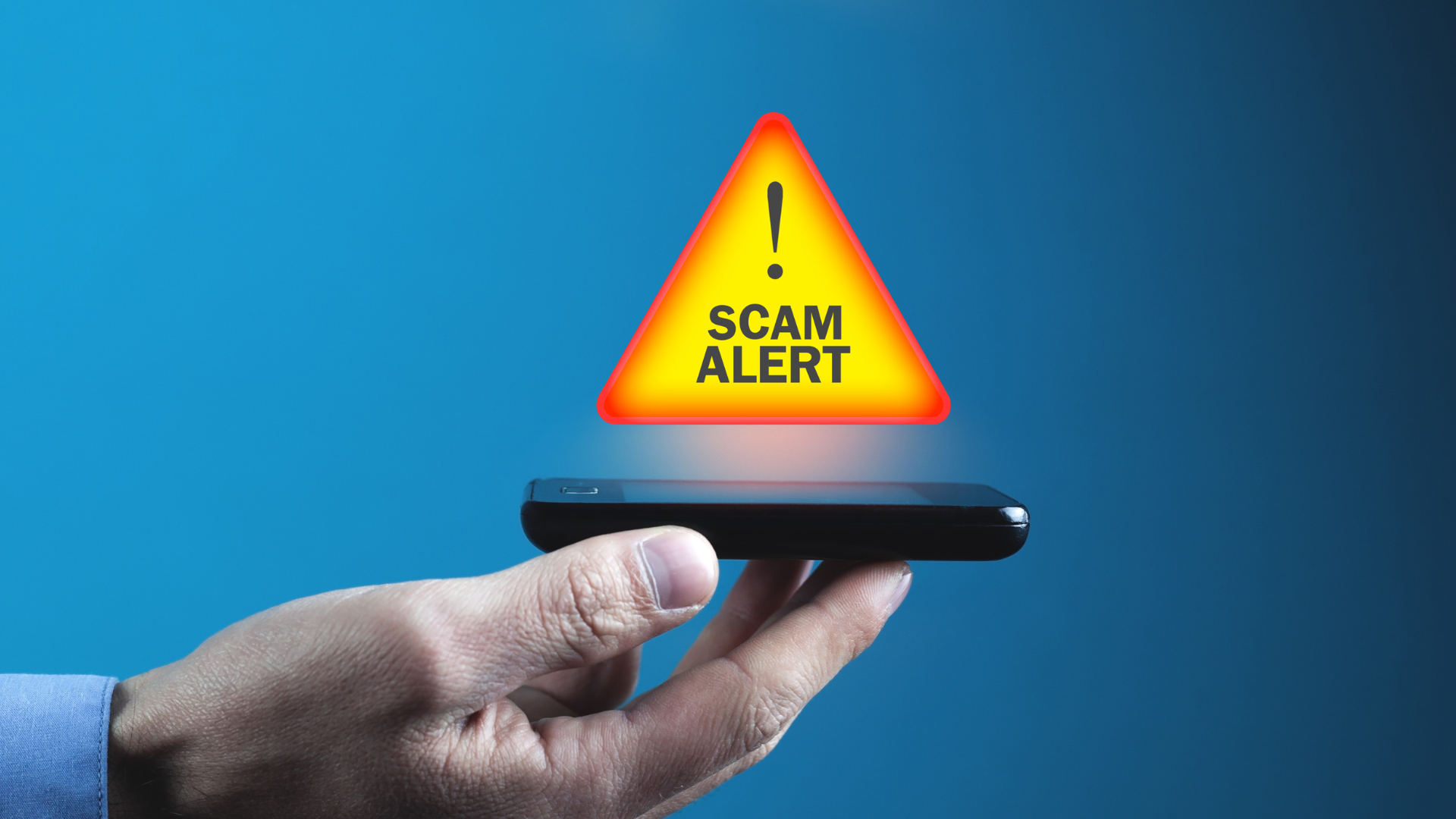 A person is holding a cell phone with a scam alert sign coming out of it.