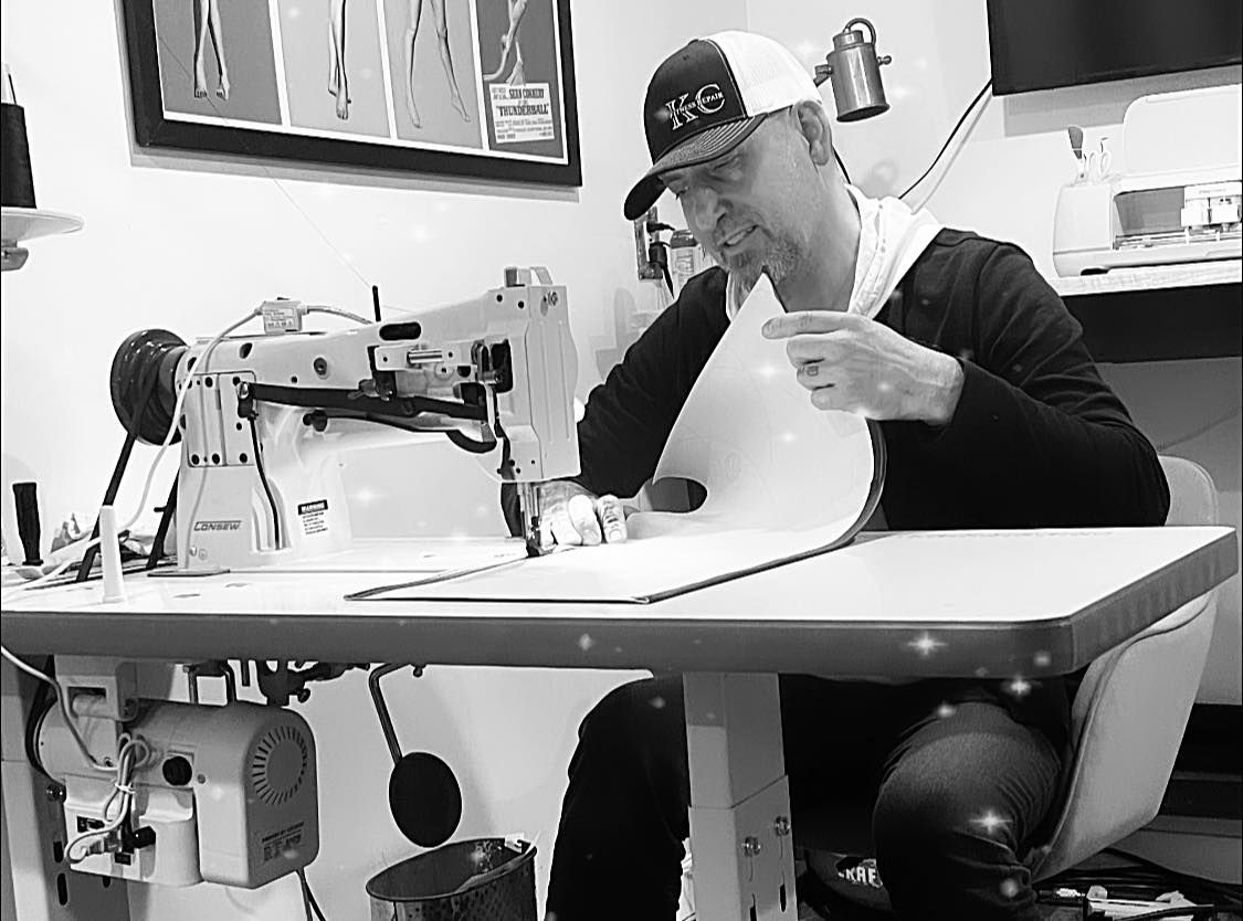 A man is sitting at a sewing machine in a black and white photo.