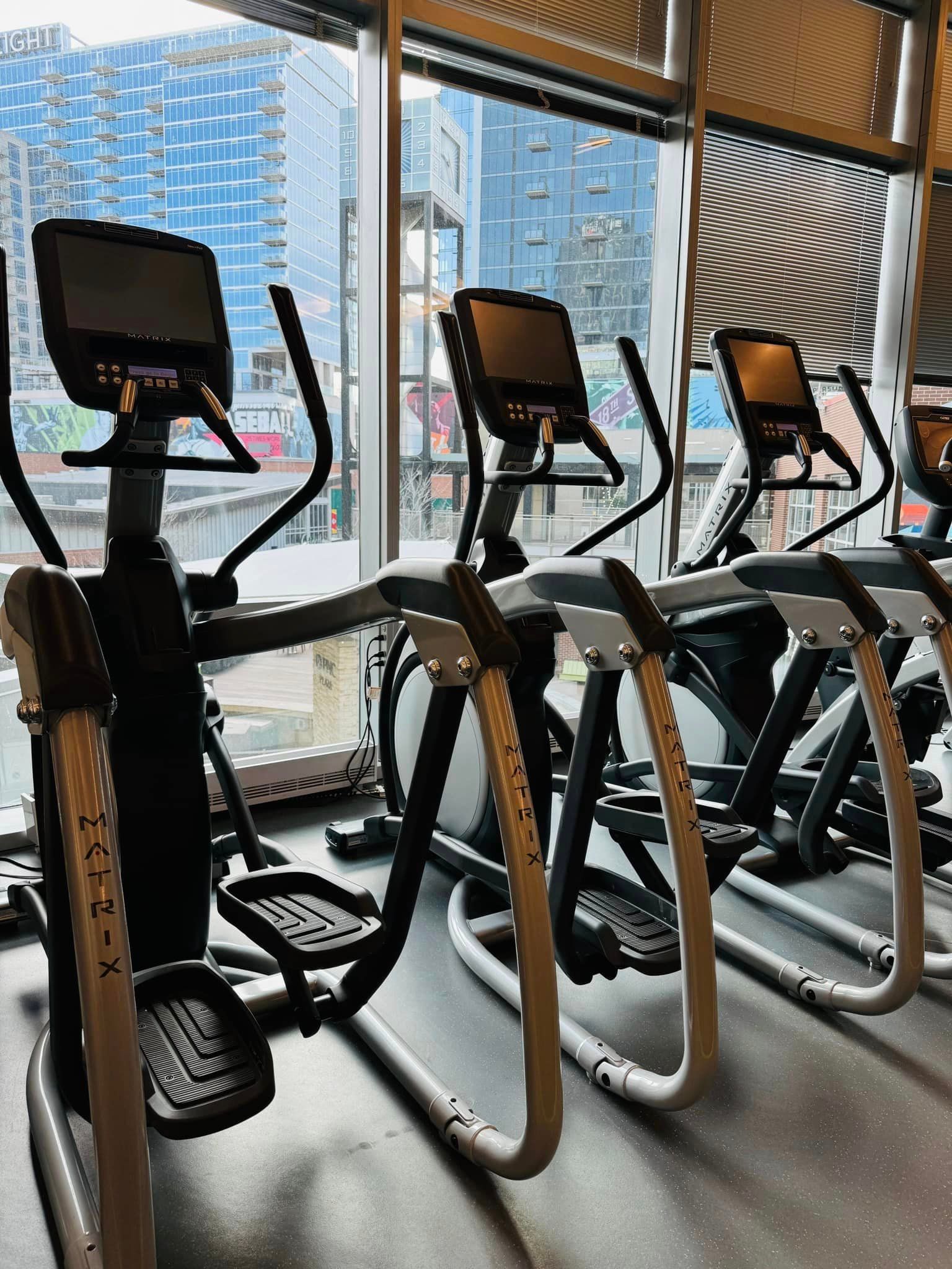 A row of ellipticals in a gym next to a window.