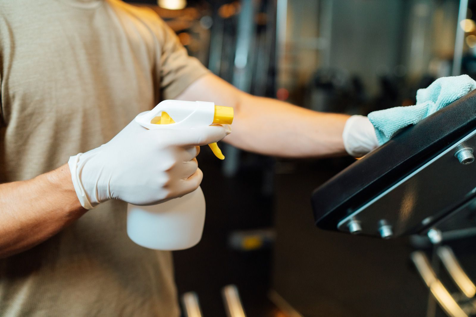 A man is cleaning a treadmill with a spray bottle and a towel.