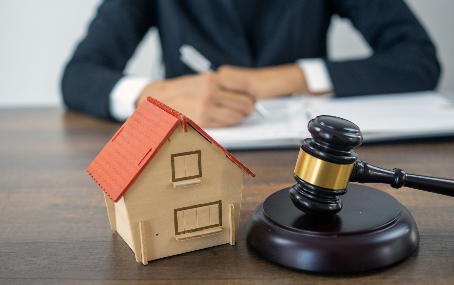 Bankruptcy lawyer at desk with gavel and house model during legal consultation.