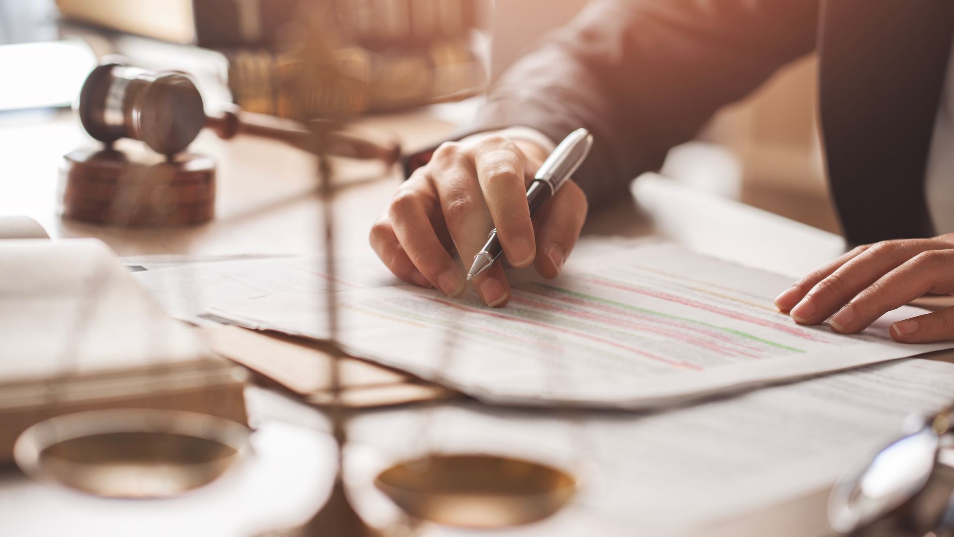Lawyer writing with gavel and justice scales nearby.