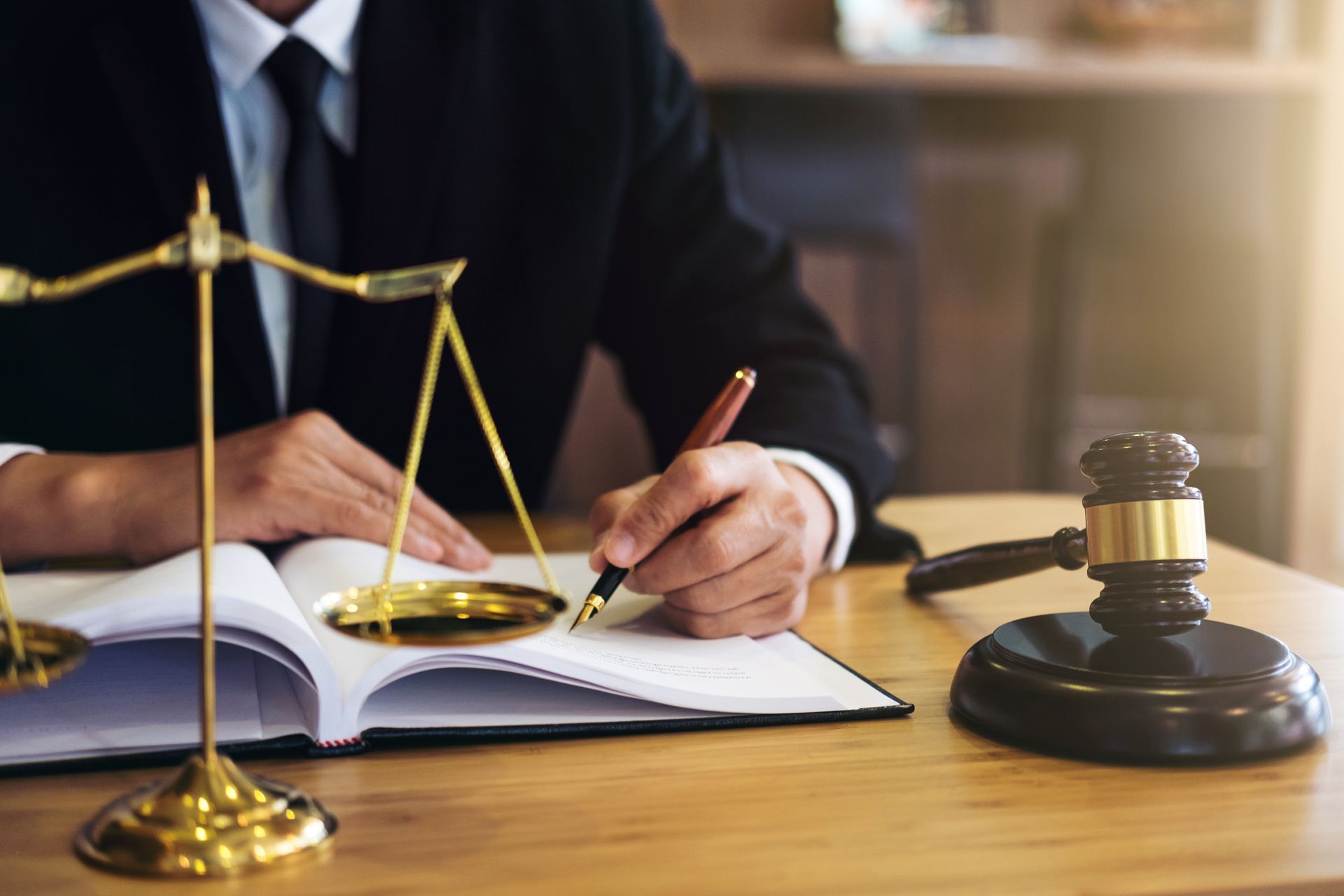 Attorney writing in legal book with scales of justice and gavel on desk in professional law office.