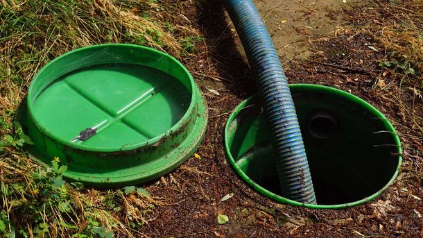 Green septic tank lid open with a blue hose inside, set in the dirt. Green septic tank lid open with a blue hose inside, set in the dirt.