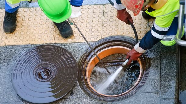Workers cleaning a manhole with high-pressure water. One worker wearing a green hard hat, the other a red one. Workers cleaning a manhole with high-pressure water. One worker wearing a green hard hat, the other a red one.
