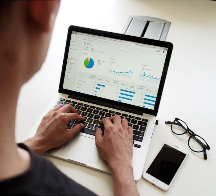 A man is typing on a laptop computer with a graph on the screen.