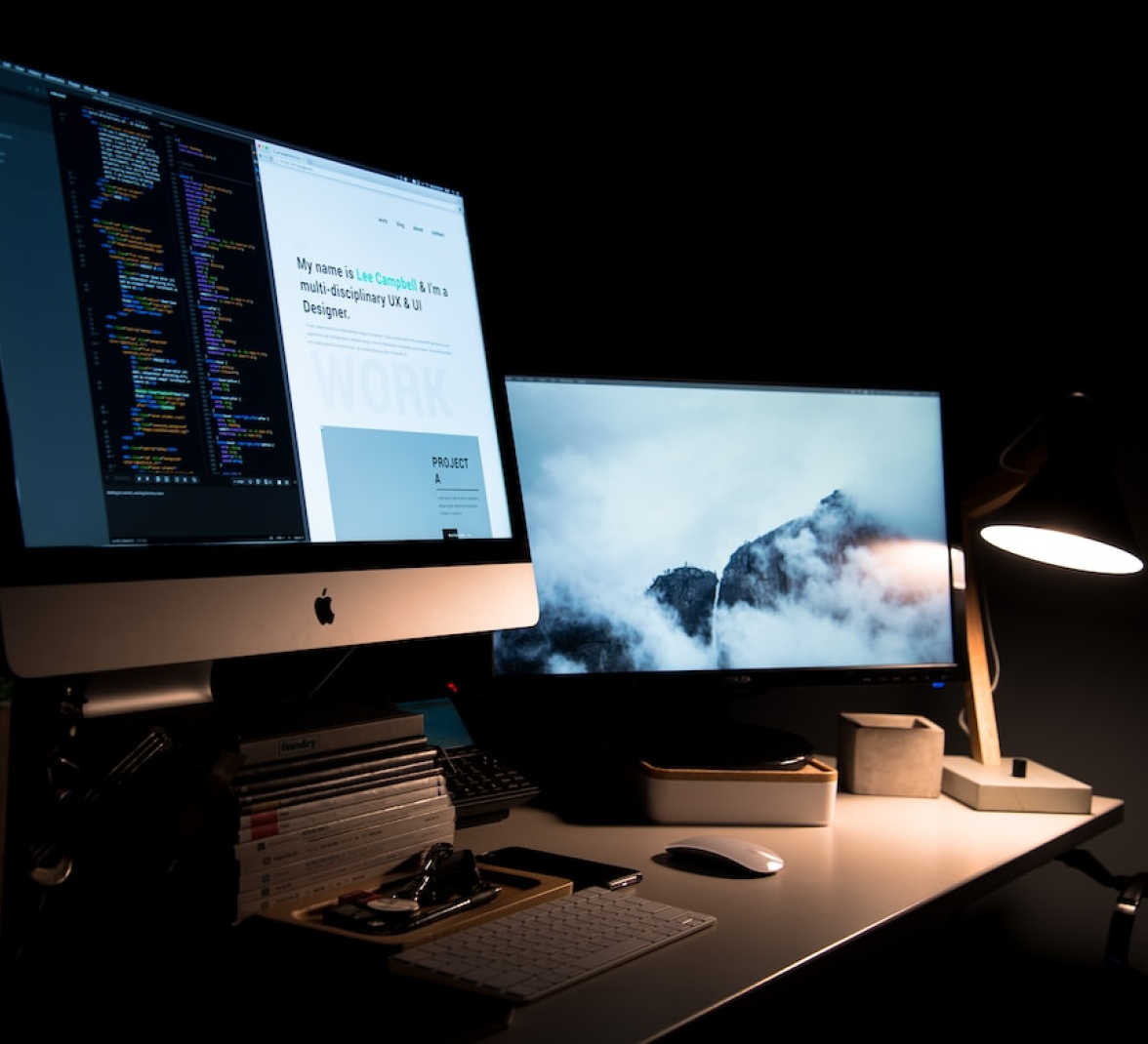 Two computer monitors are sitting on a desk in a dark room.