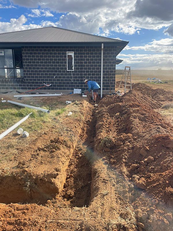 A Man Is Digging a Hole in The Dirt in Front of A House — BJB Plumbing & Gasfitting in Dubbo, NSW