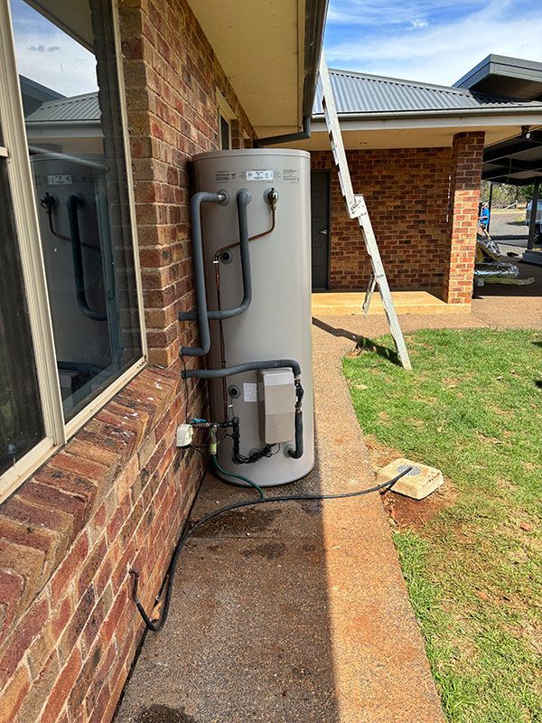 A Water Heater Is Attached To The Side Of A Brick House — BJB Plumbing & Gasfitting in Dubbo, NSW