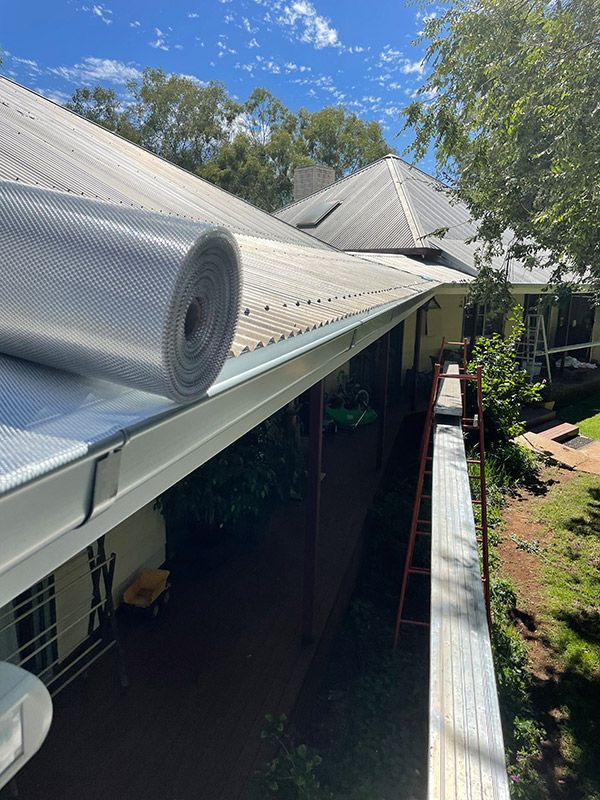 A Roll Of Insulation Is Sitting On The Gutter Of A House — BJB Plumbing & Gasfitting in Dubbo, NSW
