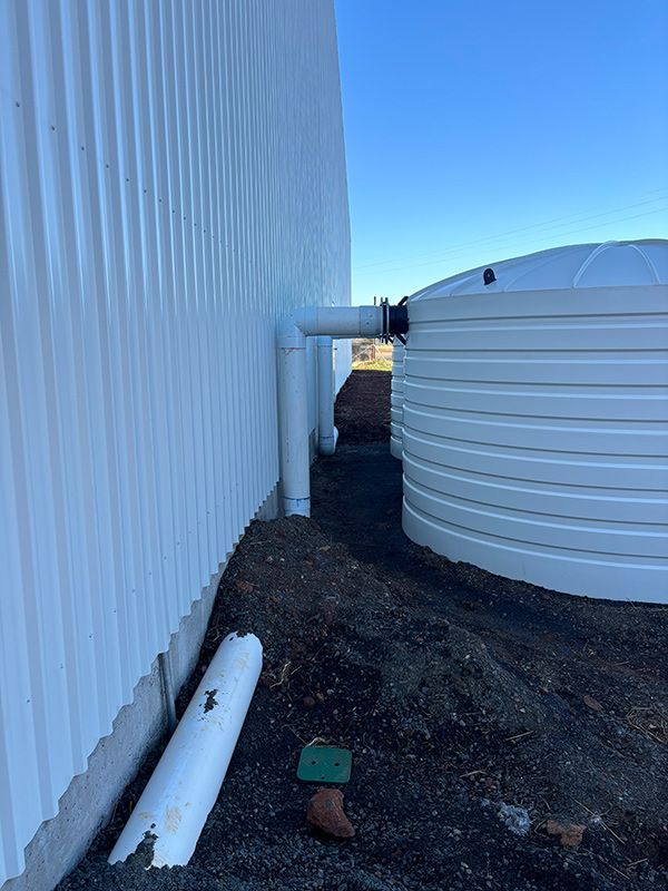 A White Water Tank Is Sitting Next to A White Building — BJB Plumbing & Gasfitting in Cobar, NSW