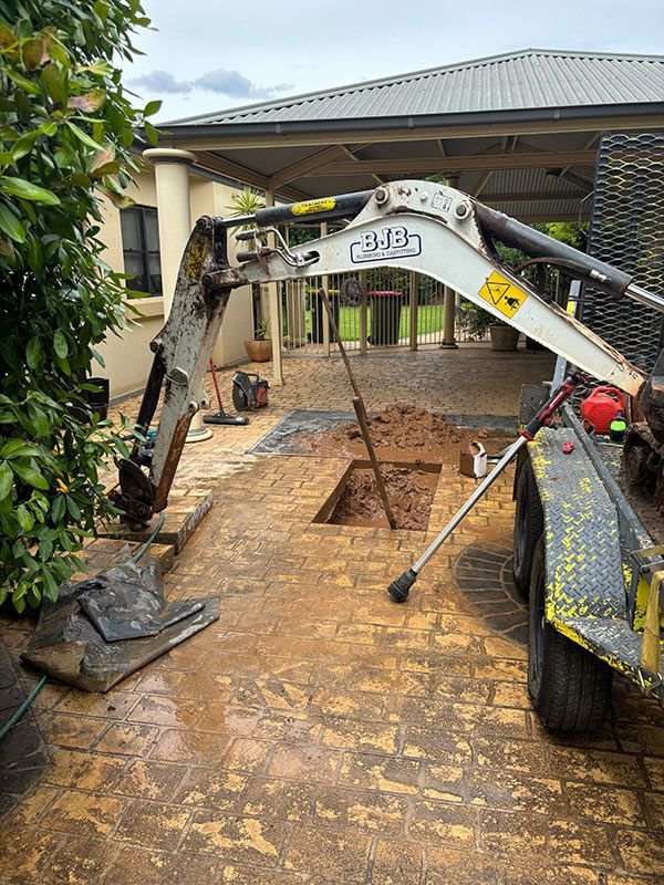 A Crane Is Digging a Hole in The Ground in Front of A House — BJB Plumbing & Gasfitting in Dubbo, NSW