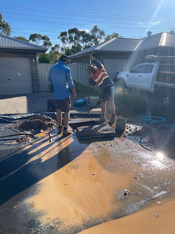 Two Men Are Working on A Muddy Driveway Next to A Truck — BJB Plumbing & Gasfitting in Dubbo, NSW