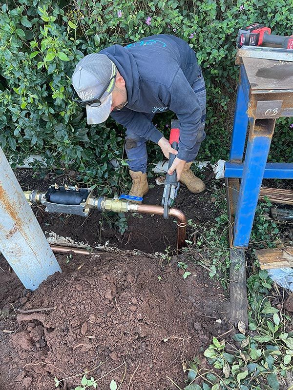 A Man Is Working On A Pipe In The Dirt — BJB Plumbing & Gasfitting in Dubbo, NSW