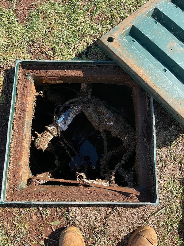A Person Is Standing In A Hole In The Ground Next To A Green Drain Cover — BJB Plumbing & Gasfitting in Dubbo, NSW