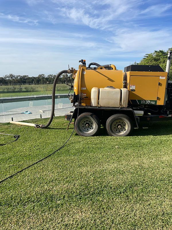 A Yellow Vacuum Truck Is Parked In A Grassy Field Next To A Pool — BJB Plumbing & Gasfitting in Dubbo, NSW
