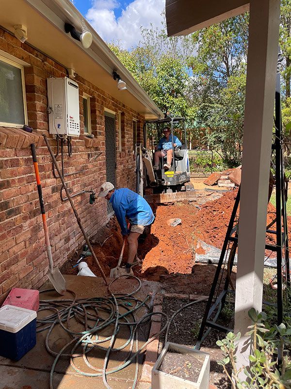 A Man Is Digging a Hole in Front of A Brick House — BJB Plumbing & Gasfitting in Dubbo, NSW