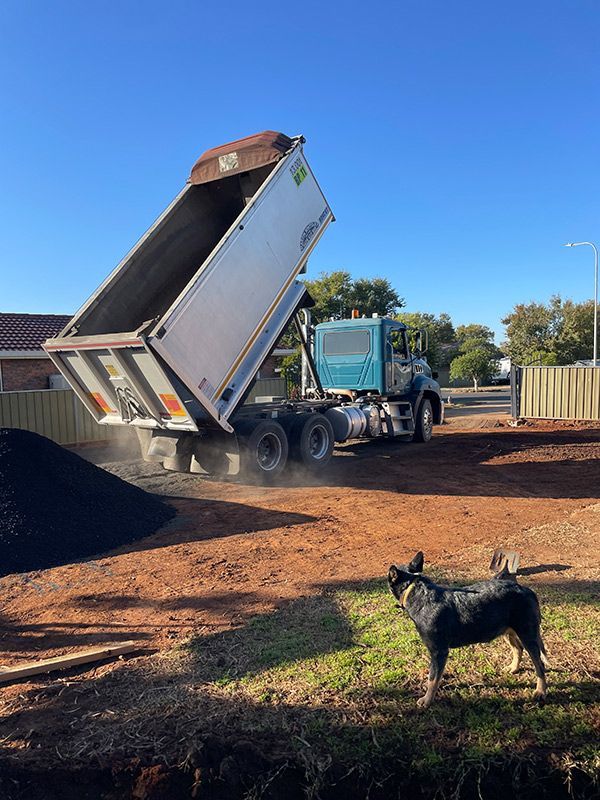 A Dump Truck Is Being Loaded with Dirt and A Dog Is Standing in Front of It — BJB Plumbing & Gasfitting in Coonabarabran, NSW