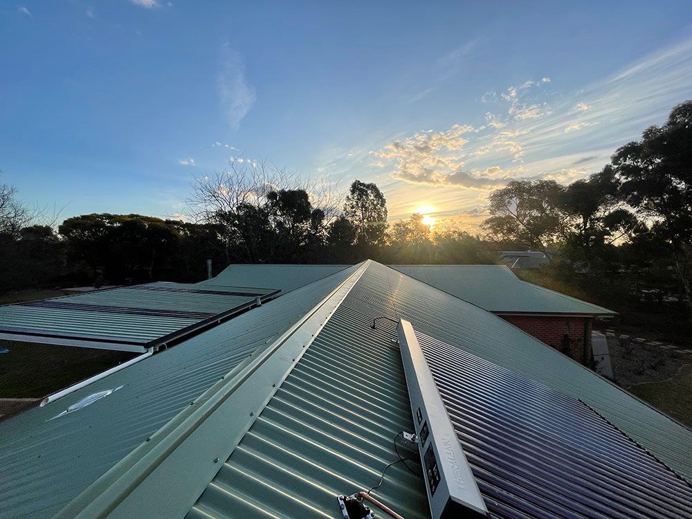 The Sun Is Setting Behind a House with A Green Roof — BJB Plumbing & Gasfitting in Dubbo, NSW