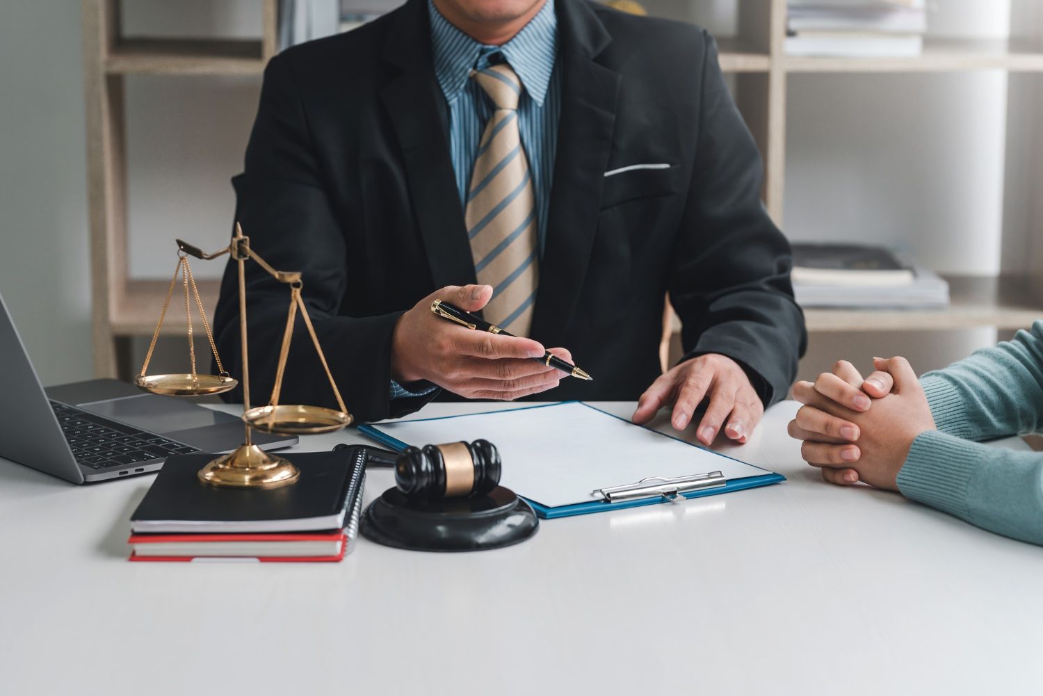 Lawyer in suit gestures to paperwork at a desk. Scales, gavel, and client seated nearby.