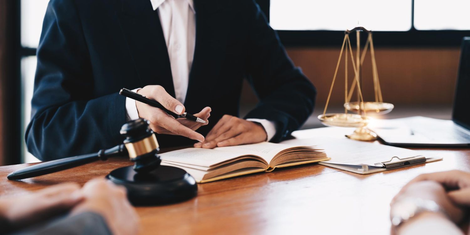 Lawyer pointing at documents during a consultation with clients, next to a gavel and scales of justice.