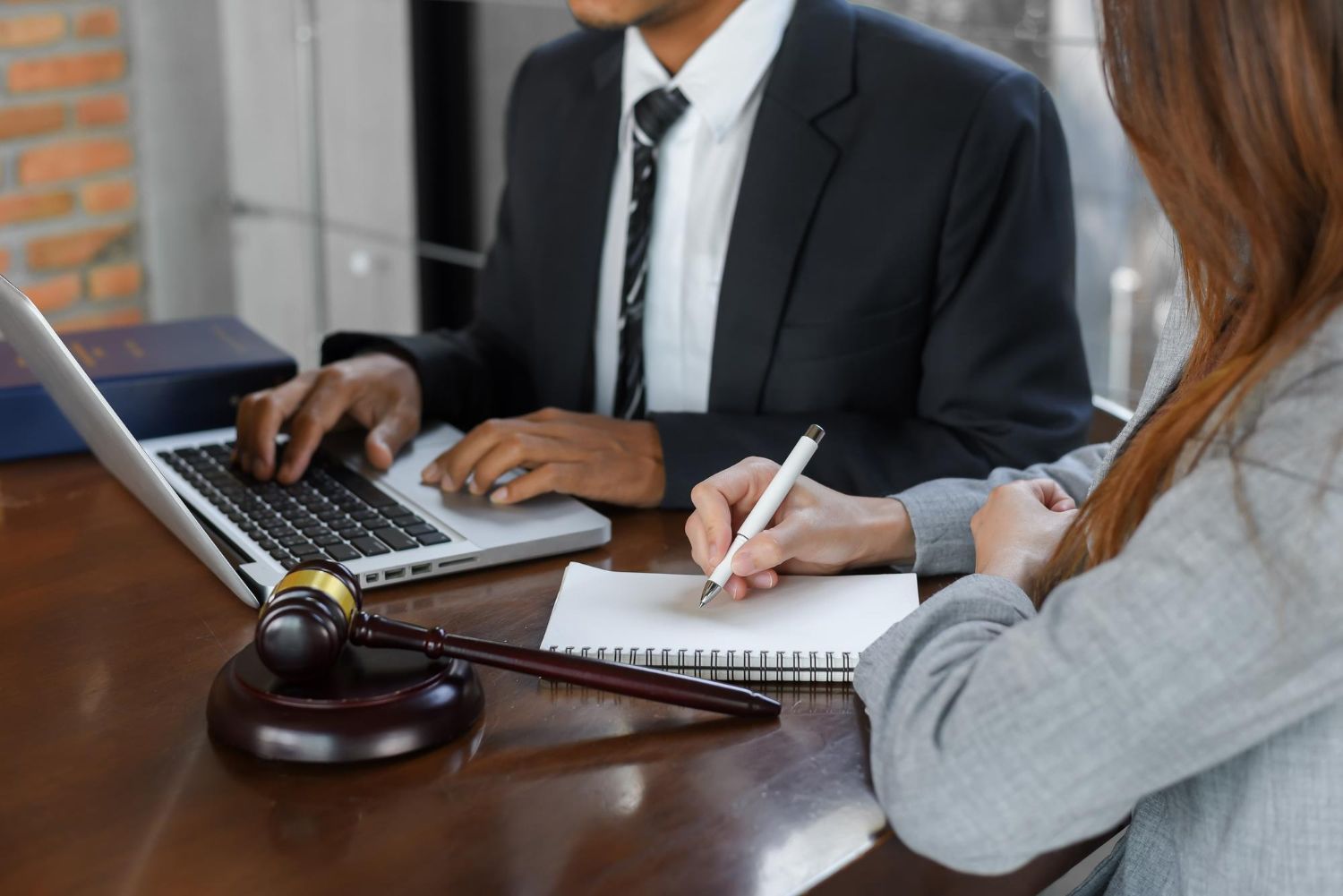 Lawyer and client at table with laptop, notes, and gavel.