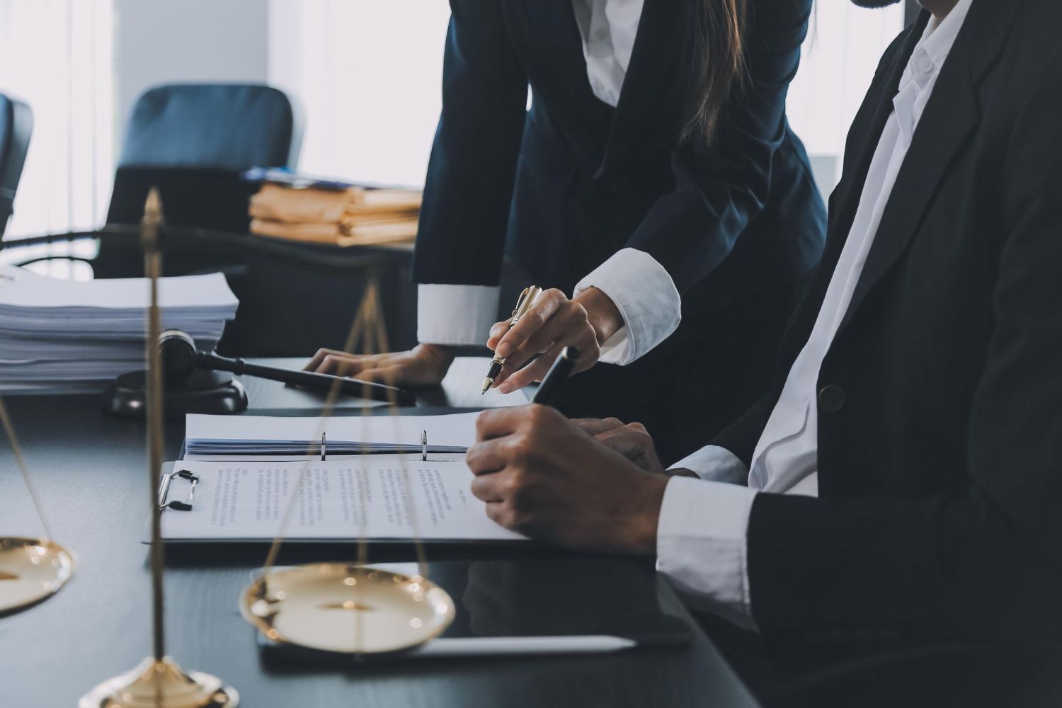 Two lawyers reviewing documents at a table; scales of justice and law books in background.