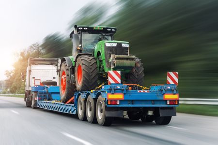 A tractor is being transported on a trailer on a highway.