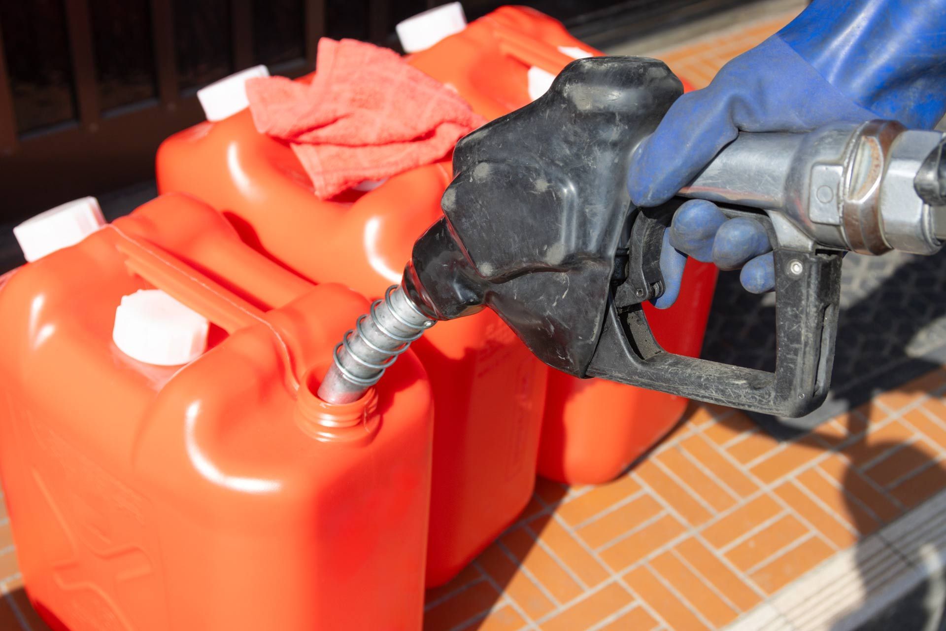 Fuel nozzle filling a red plastic gas can outdoors