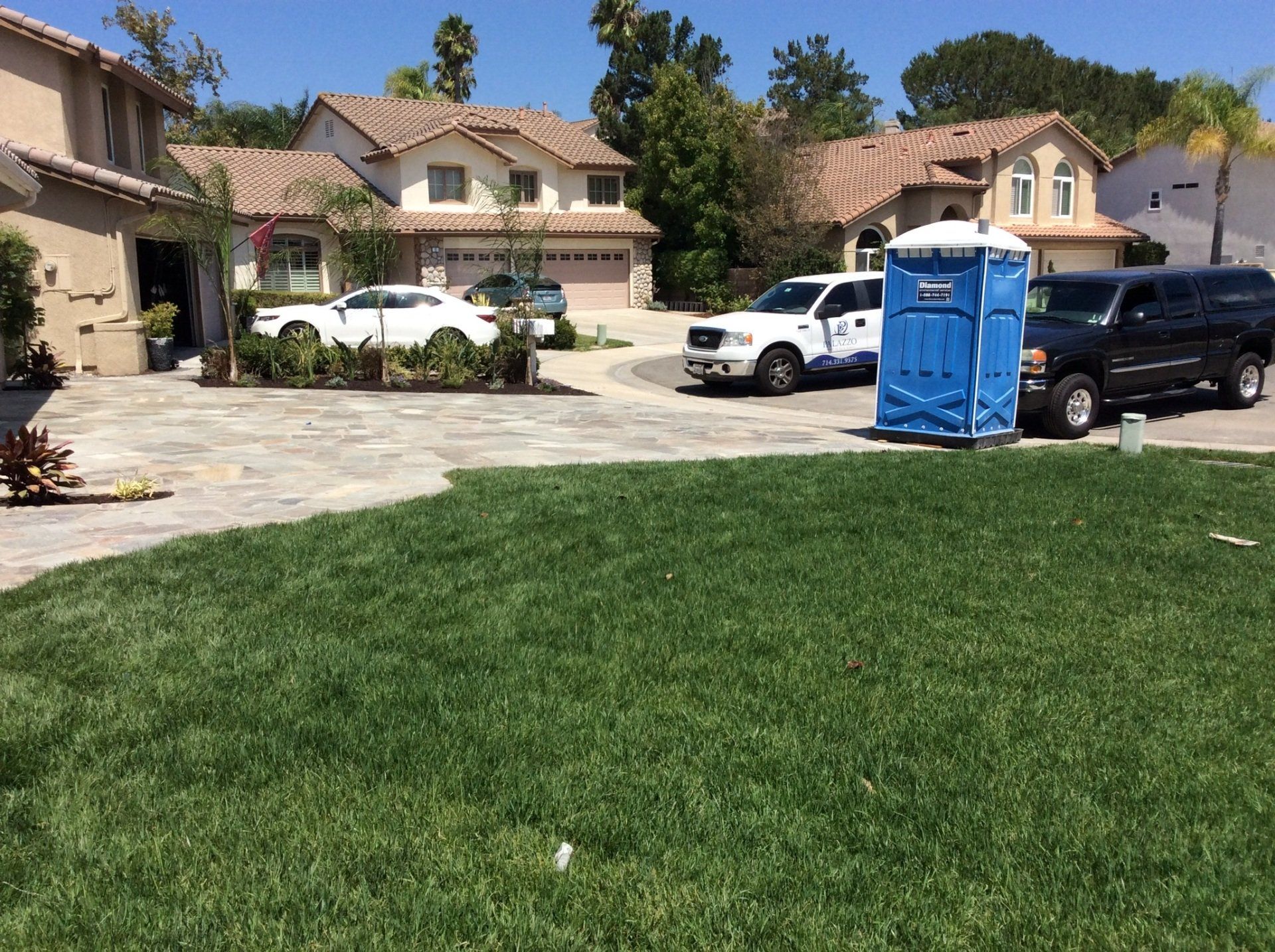 A blue portable toilet is parked in front of a house