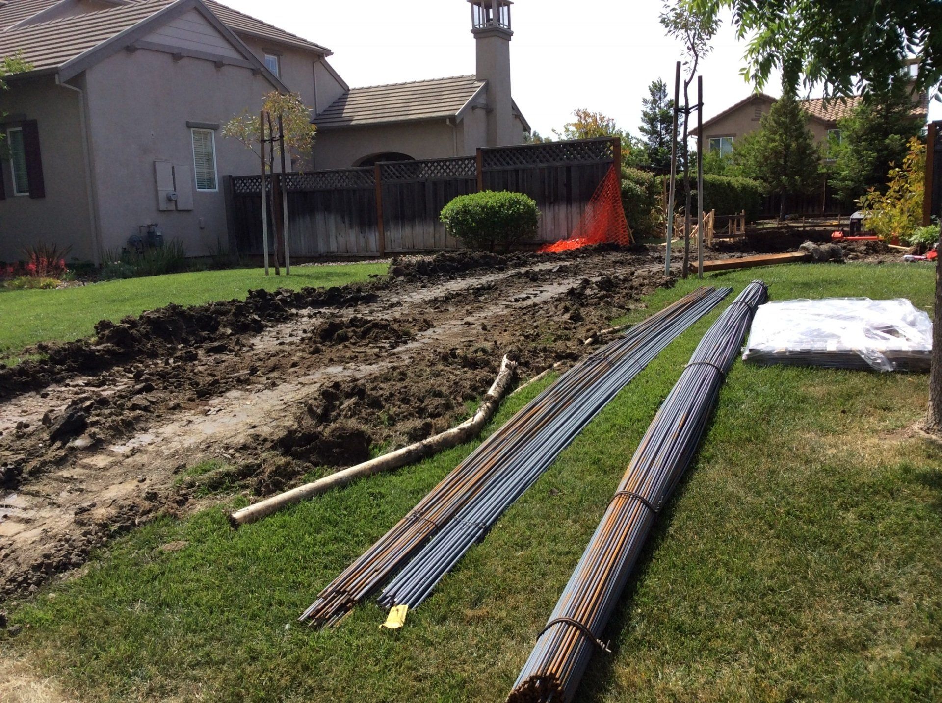 A lot of pipes are laying on the grass in front of a house