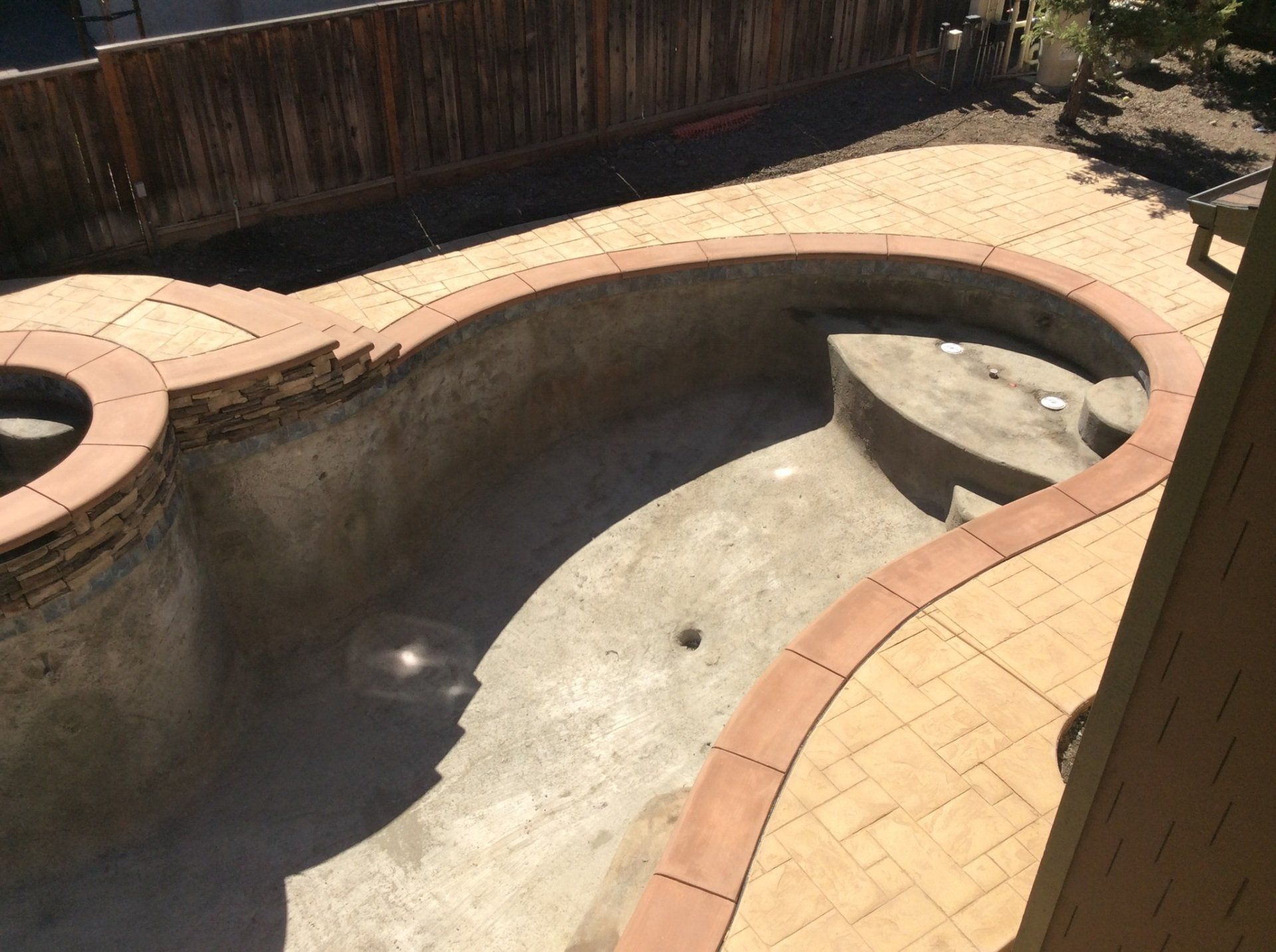 An empty swimming pool with a wooden fence in the background
