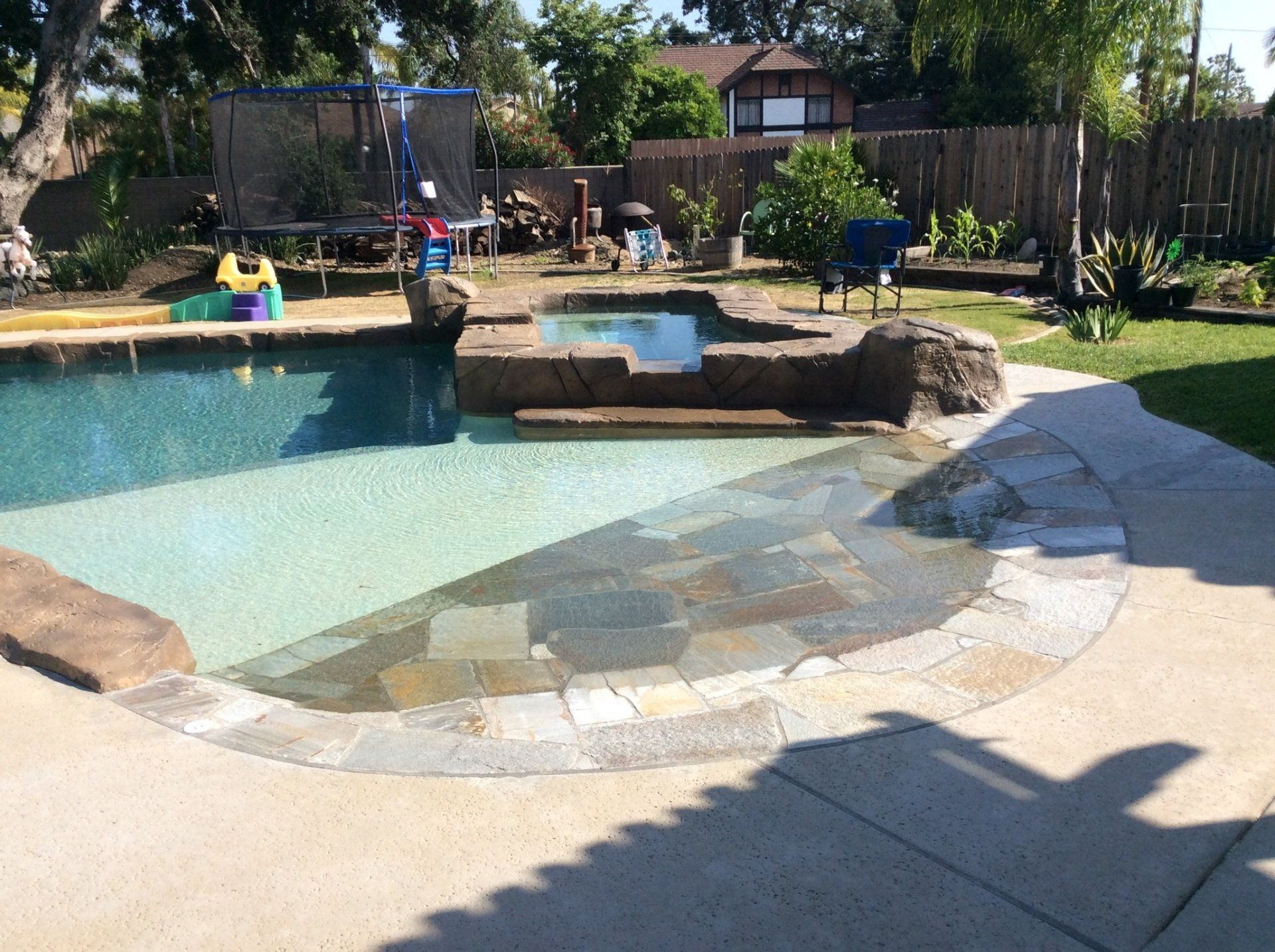 A large swimming pool in a backyard with a patio in front of it