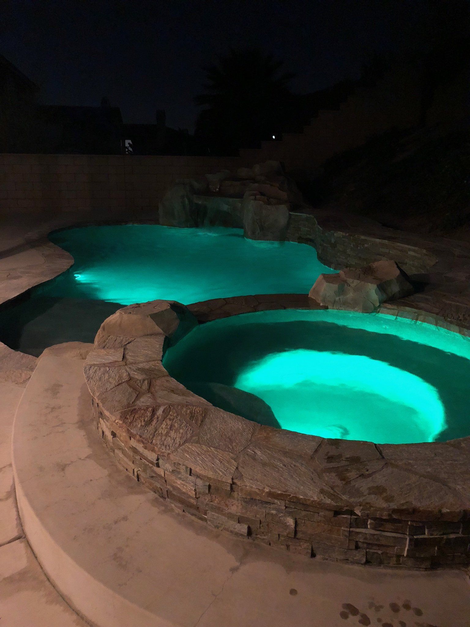 Two swimming pools are lit up at night with green lights.