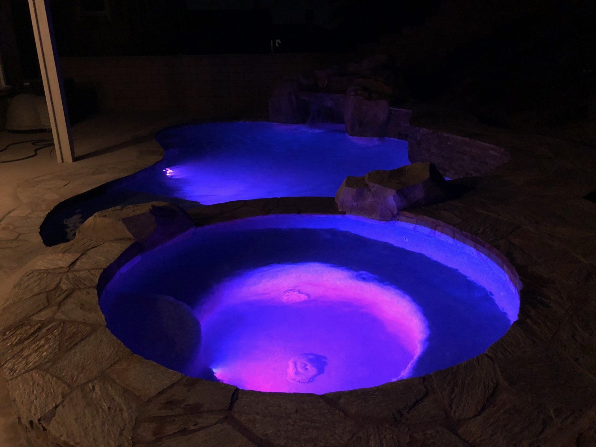 Two hot tubs are lit up at night with purple lights.