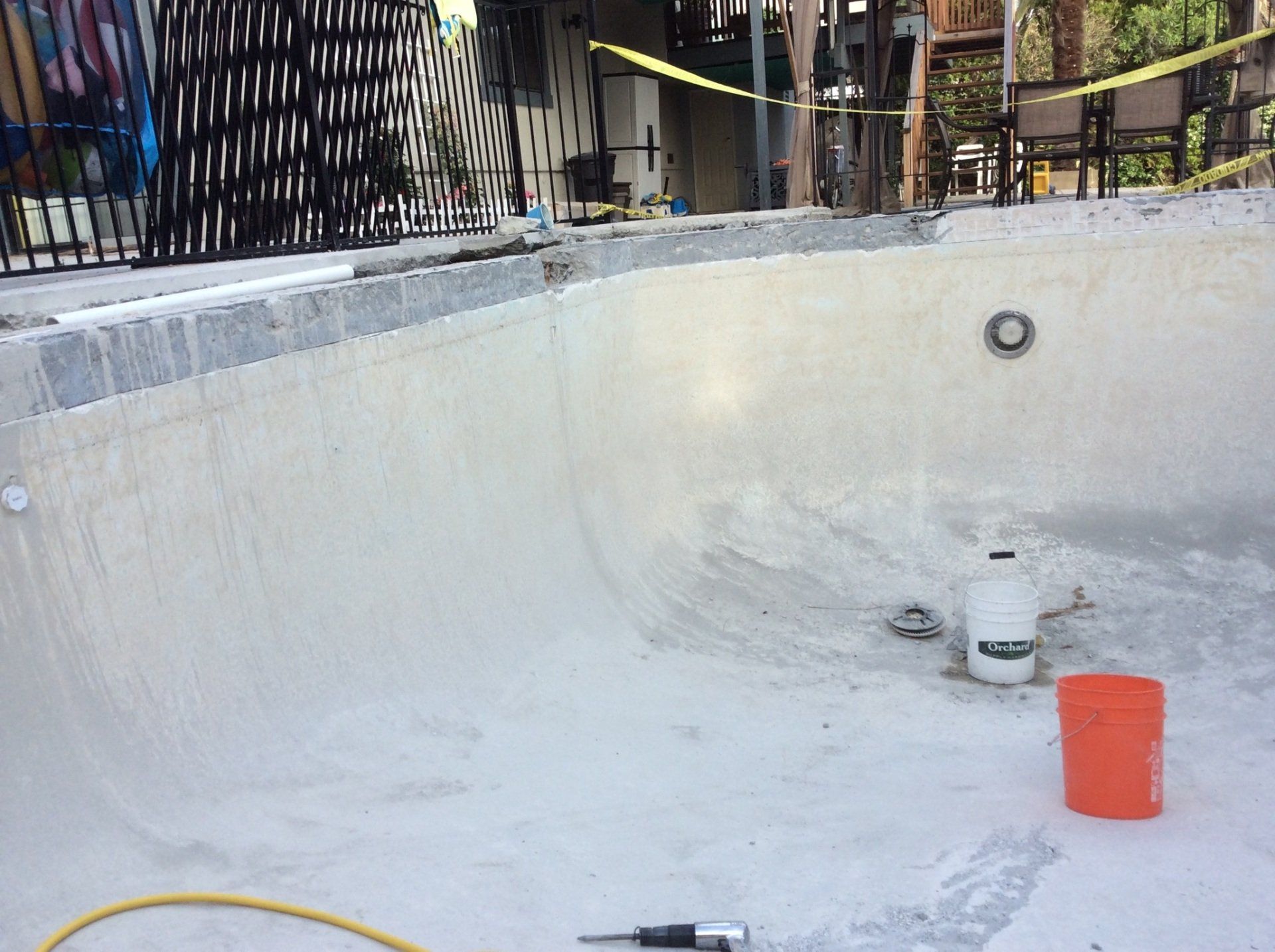 An empty swimming pool with a hose and a bucket on the ground.