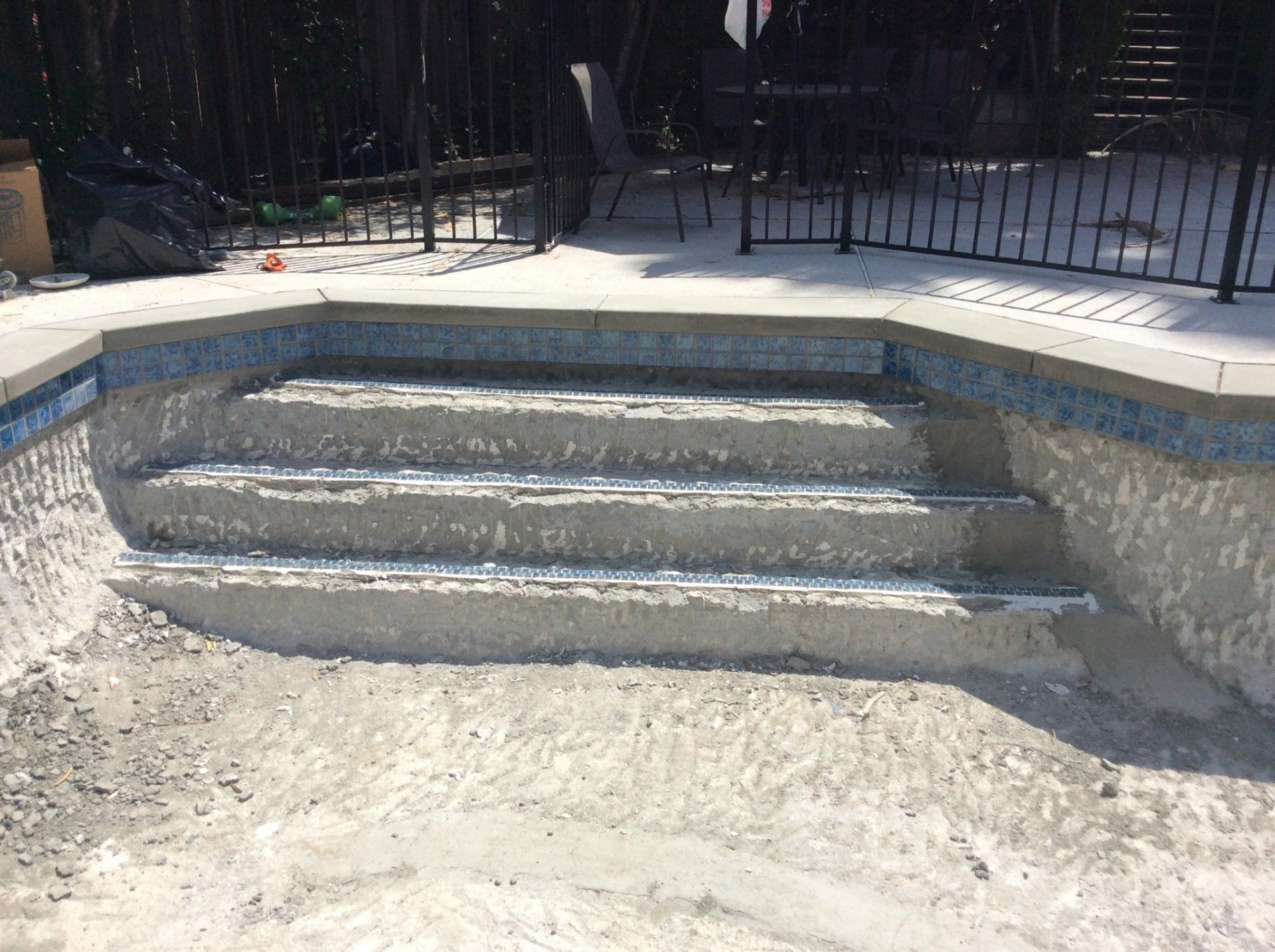 A swimming pool with stairs and a fence in the background.