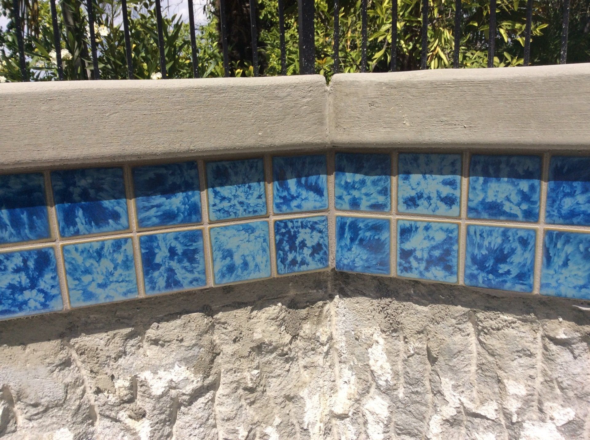 A swimming pool with blue tiles and a fence in the background.