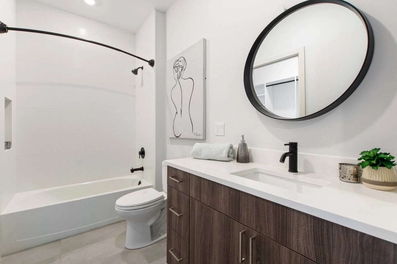 Modern bathroom with a bathtub, toilet, wood vanity, and round mirror