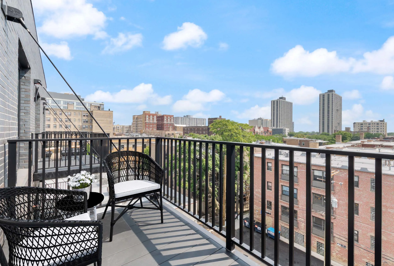Rooftop terrace with black chairs overlooking a city skyline under a blue sky