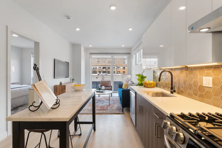 Bright modern galley kitchen with white cabinets, marble island, wood floors, and stainless steel appliances