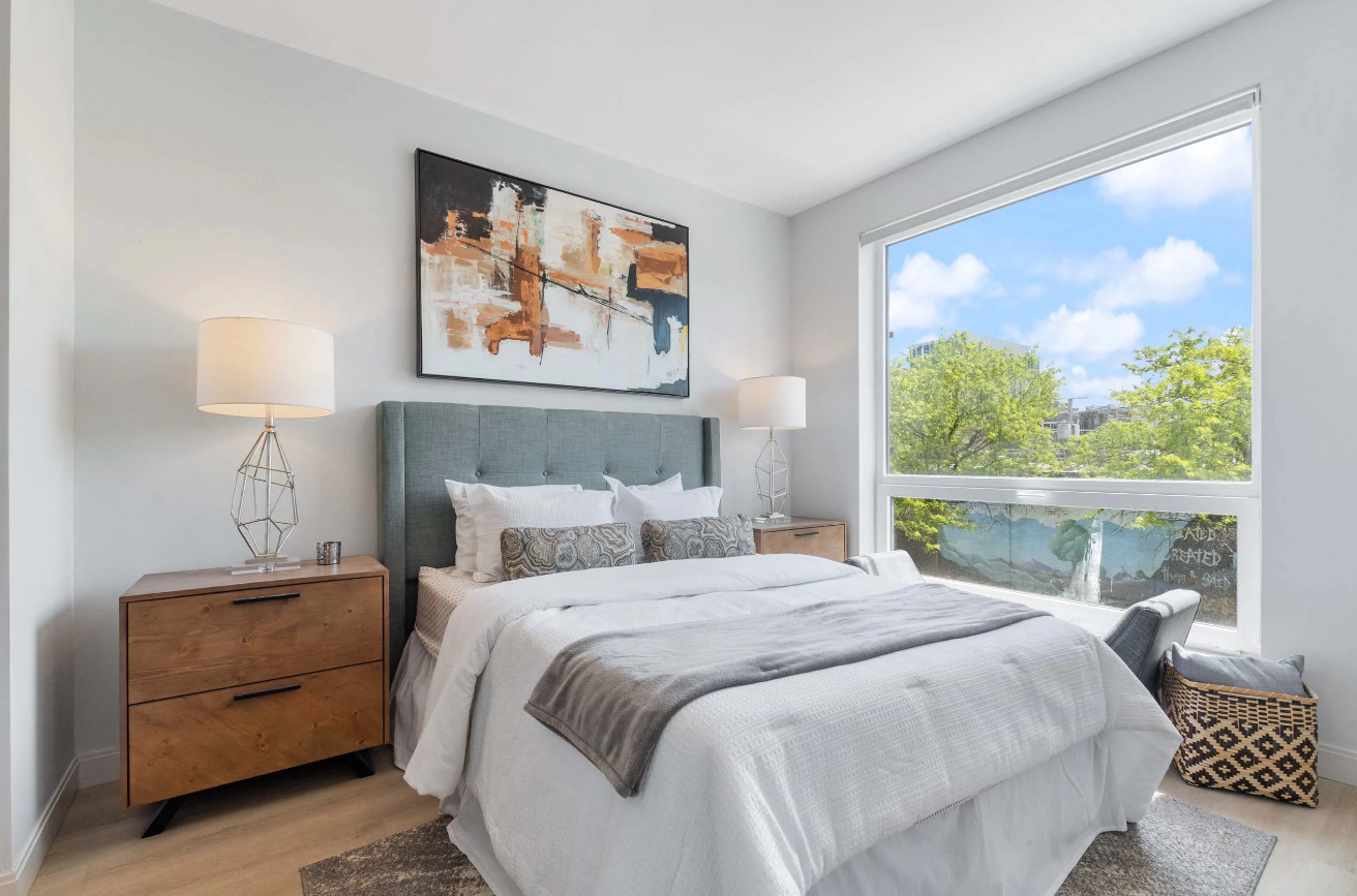 Modern bedroom with gray bed, wood nightstands, and a large window overlooking trees