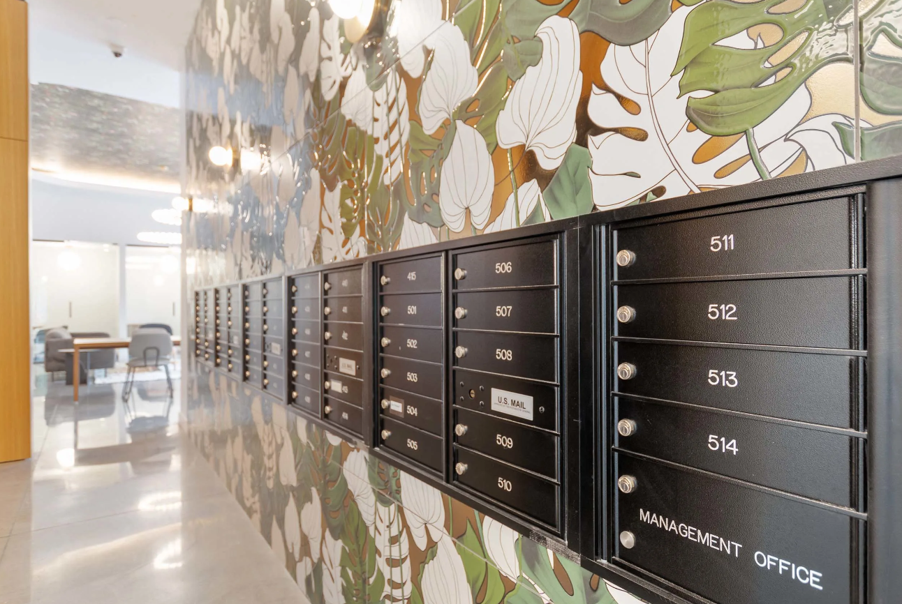 Wall of black apartment mailboxes in a bright lobby with patterned floral mural