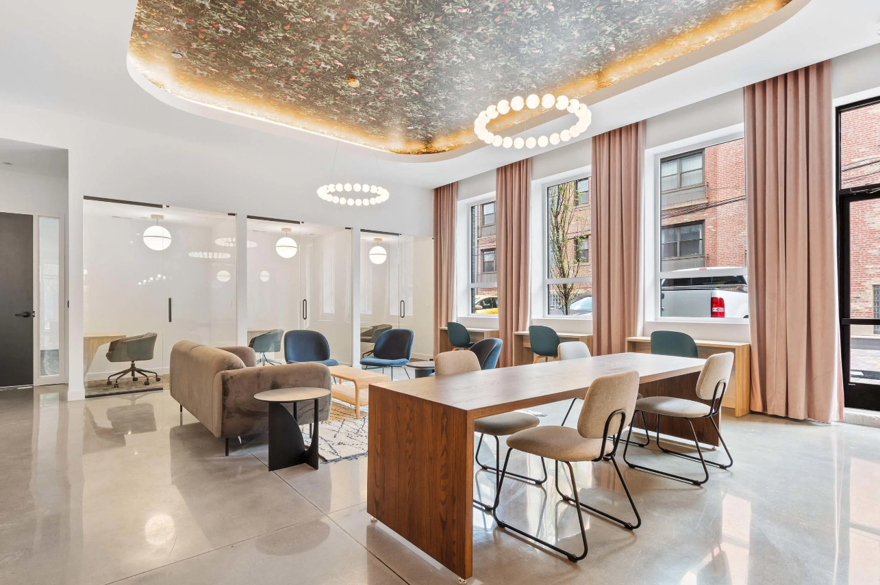 Modern office lounge with beige chairs, wooden tables, glass walls, and circular ceiling lights