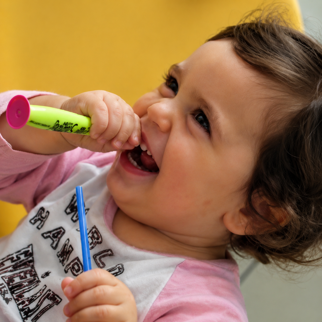 Bambino sorridente che tiene un pennarello verde alla bocca su sfondo giallo