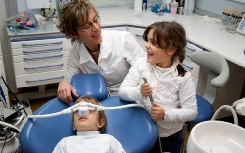 Un dentista visita un bambino mentre un altro bambino osserva in uno studio dentistico.