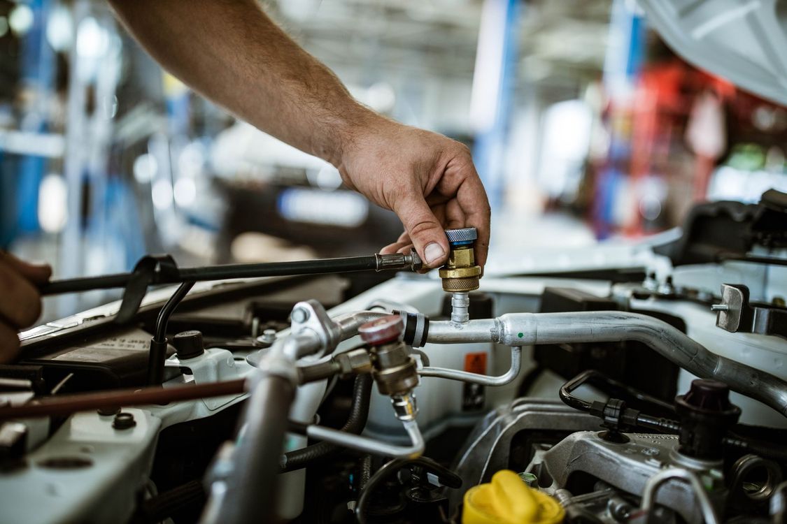Mano di un meccanico al lavoro sul motore di un'auto in un'officina.