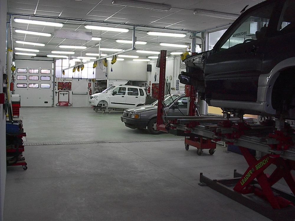 L'interno di un'officina con diversi veicoli, tra cui uno sollevato su un ponte sollevatore. Luci fluorescenti illuminano lo spazio.