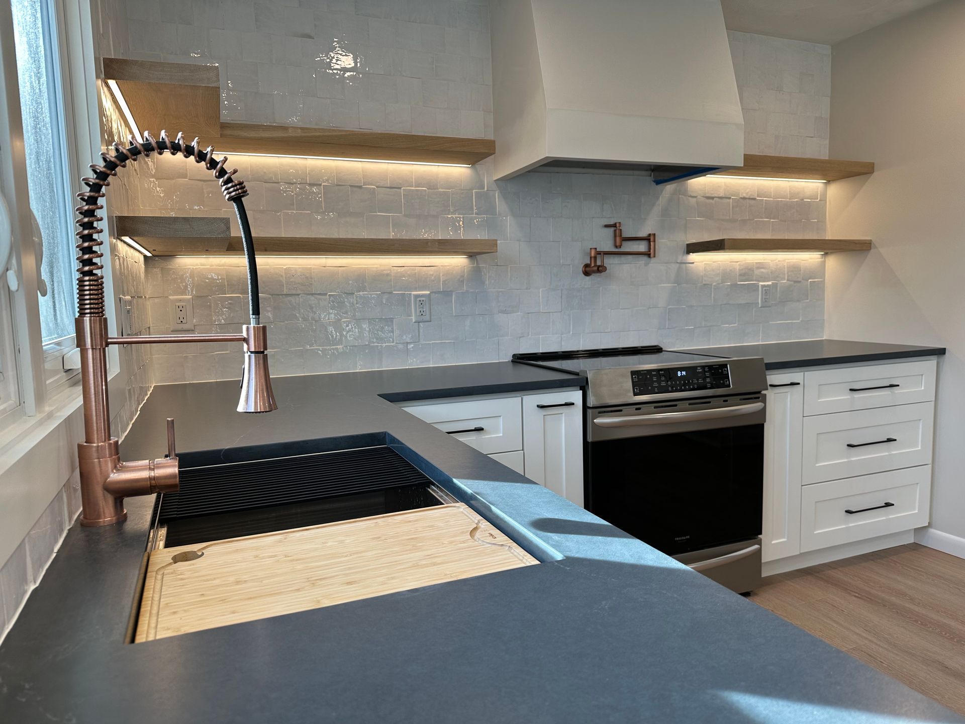 Modern kitchen with copper faucet, white cabinets, and floating shelves with under-cabinet lighting.